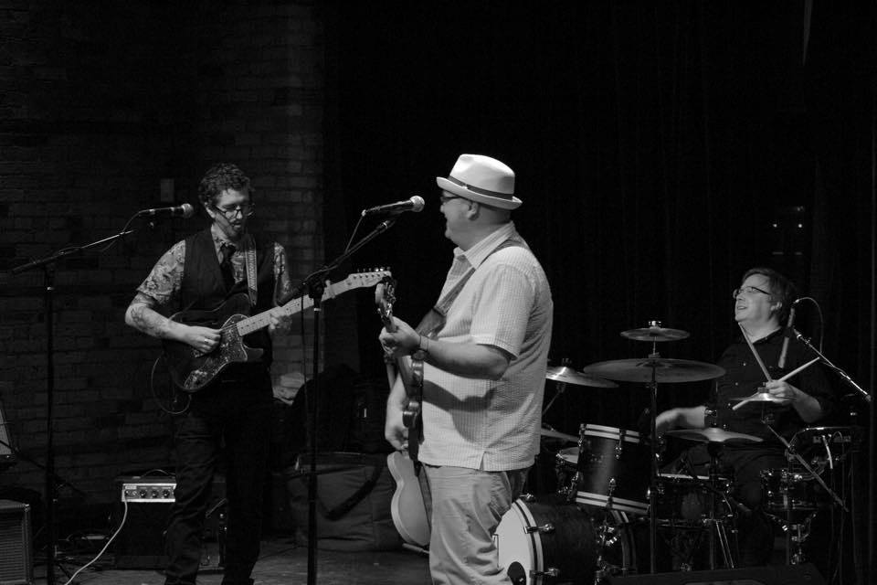 Black-and-white shot of a three-piece band performing on a dimly lit stage.