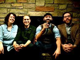 Four people sitting in front of a stone fireplace, smiling at the camera.