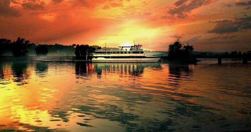 A boat floats on calm, reflective water under a bright orange sunset sky.