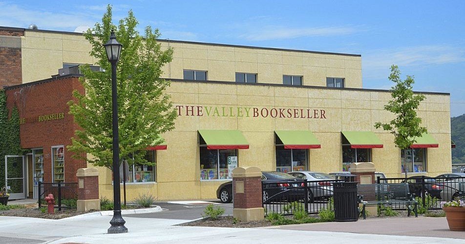 The exterior of The Valley Bookseller, a brick and yellow building with green awnings and parked cars in front.