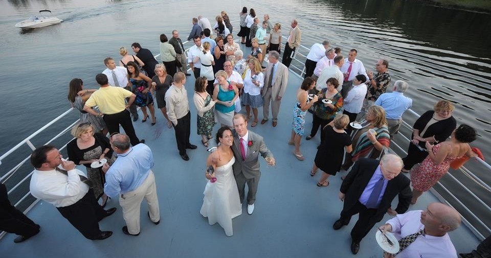 A high-angle view of a wedding party socializing on the deck of a boat moving on the water.
