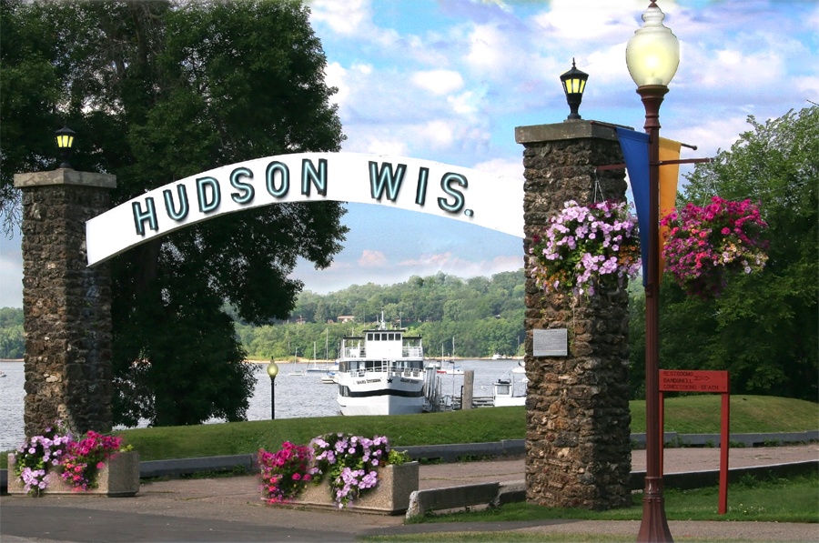 An arched sign reading "HUDSON WIS." spans two stone pillars near a river with a boat, flanked by flowers and lamps.