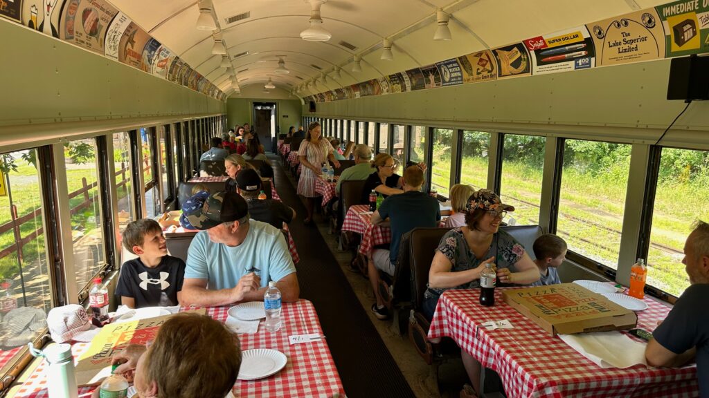 People eat at tables with red checkered tablecloths inside a vintage passenger train car.