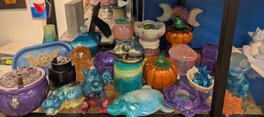 An assortment of colorful, uniquely shaped resin or ceramic decorative figures and containers on a shelf.