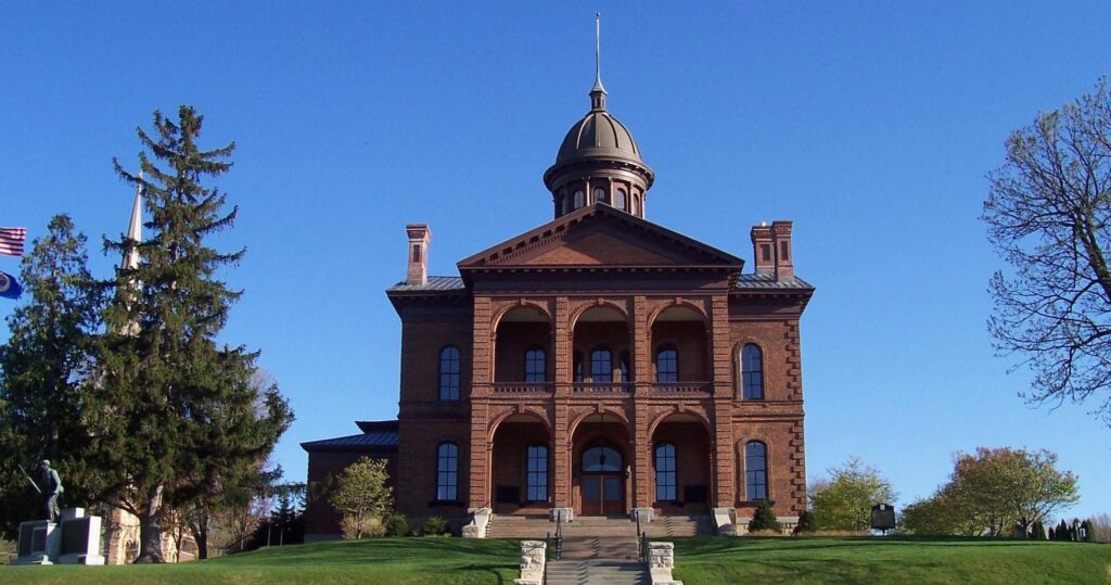 A historic brick courthouse building with a central dome, viewed from the front against a clear blue sky.