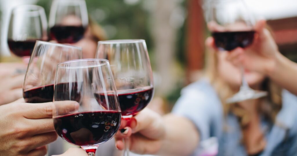 Close-up of several people holding up wine glasses of red wine for a toast.
