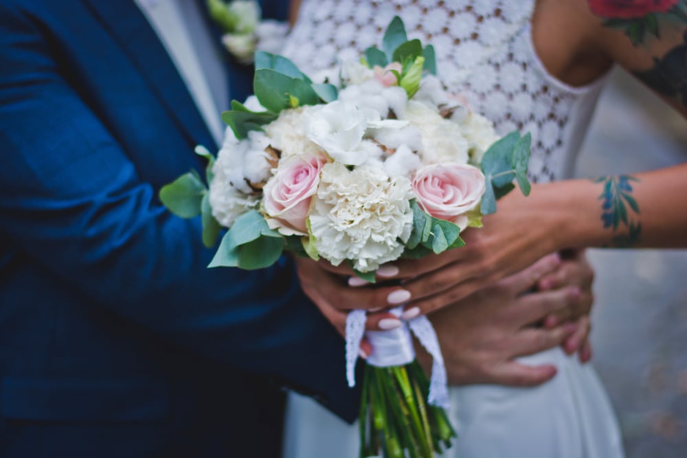 A couple embraces, holding a bouquet of white and pink roses tied with a white ribbon.