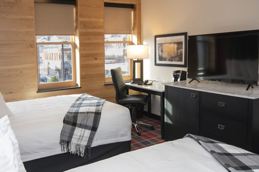 A hotel room with two beds, wood-paneled walls, a desk with a chair, and a television on a dresser.