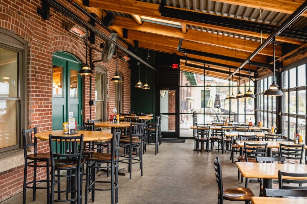 A rustic indoor patio with wooden beams, brick walls, and multiple dining tables with black chairs.