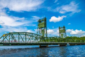Take a Ride on the Stillwater River Boats 1 A green vertical-lift truss bridge stands over a blue river against a bright blue sky with white clouds.