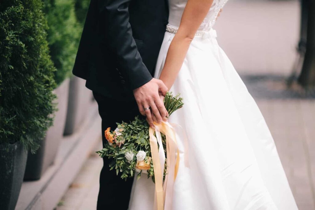 A bride and groom stand close together, their joined hands holding a small bouquet of greenery and flowers. Stillwater wedding venues in Minnesota