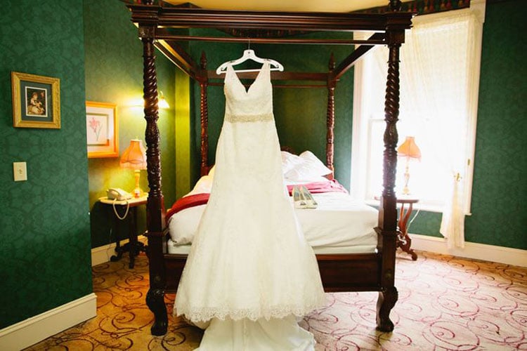 Wedding dress displayed in one of our historic suites at Water Street Inn. Dark wood canopy bed, hunter green walls, and white bedding.